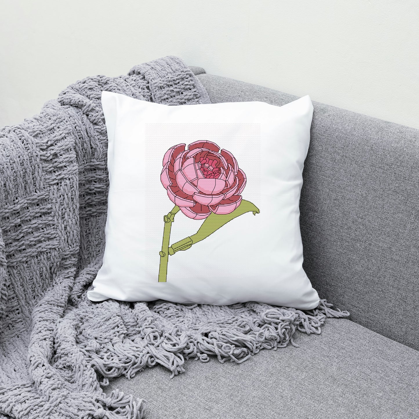 White pillow with a pink flower design on a gray couch with a gray blanket.