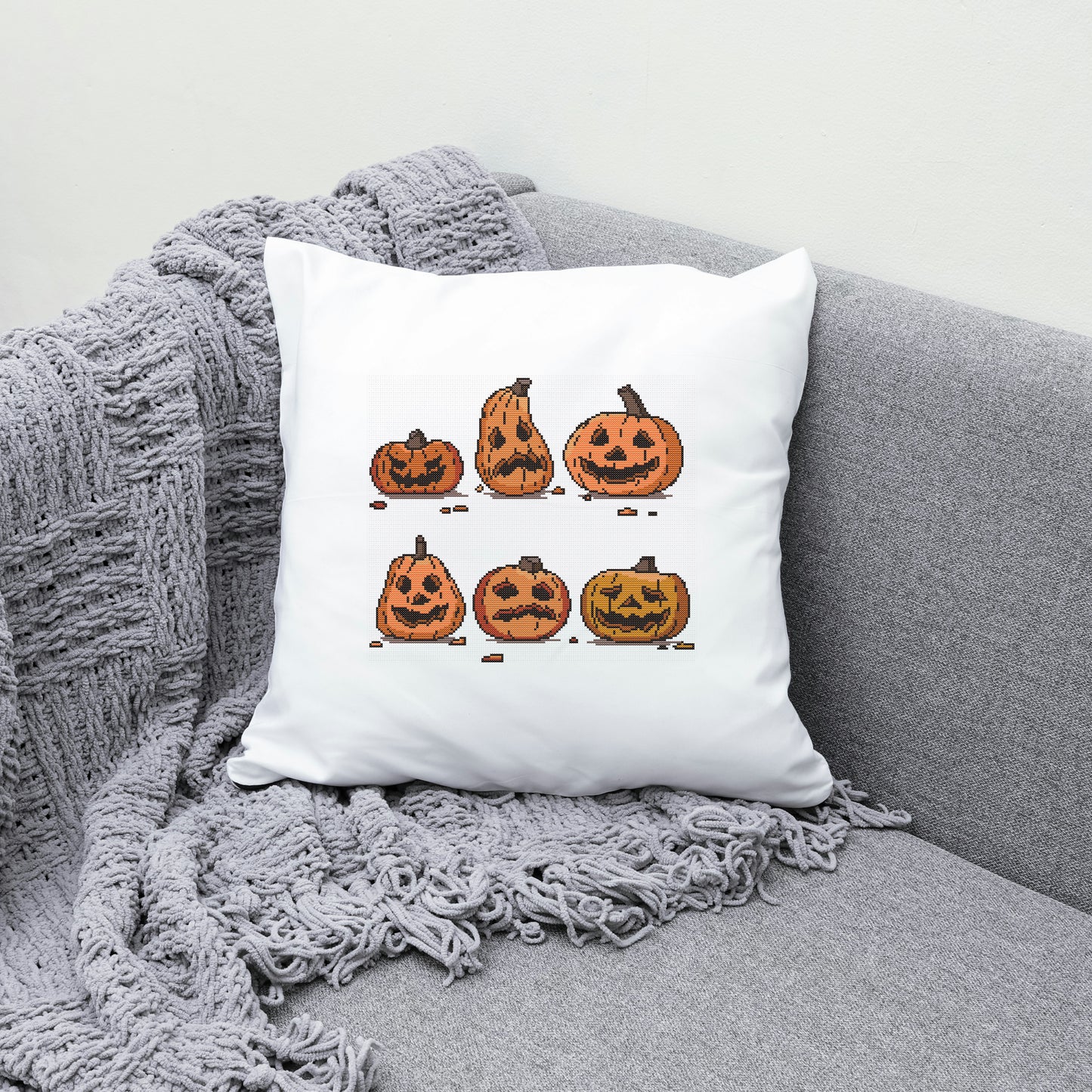 White pillow with Halloween-themed pumpkins design on a gray couch.