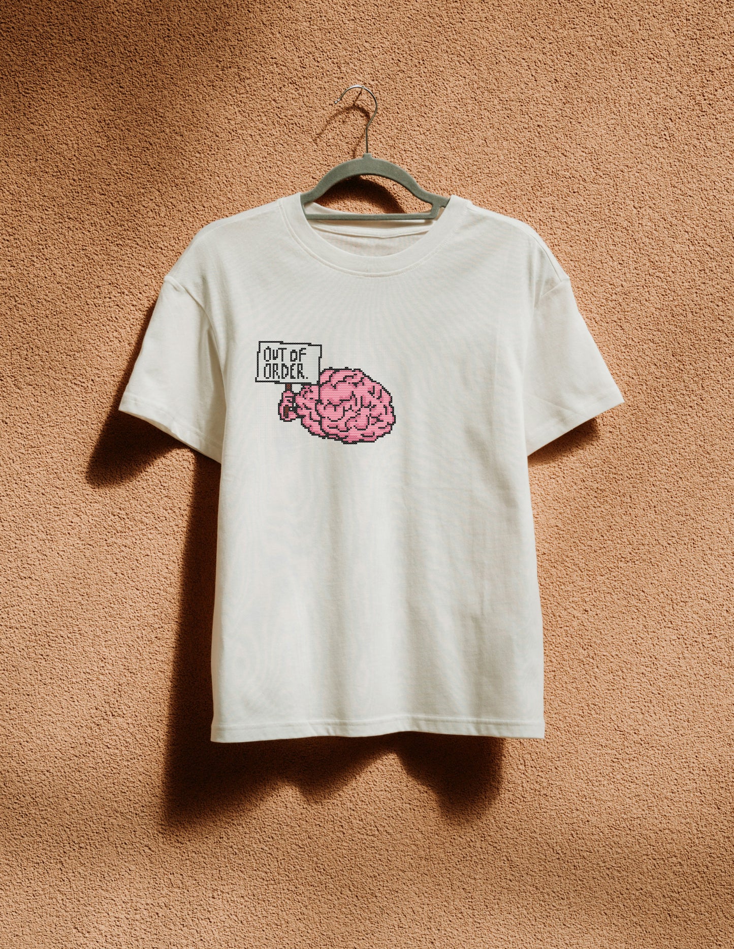 White t-shirt with a pink brain graphic and text on a beige wall