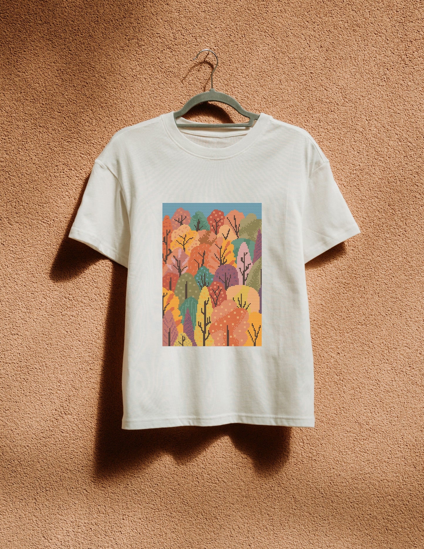 White t-shirt with a colorful forest design on a beige wall