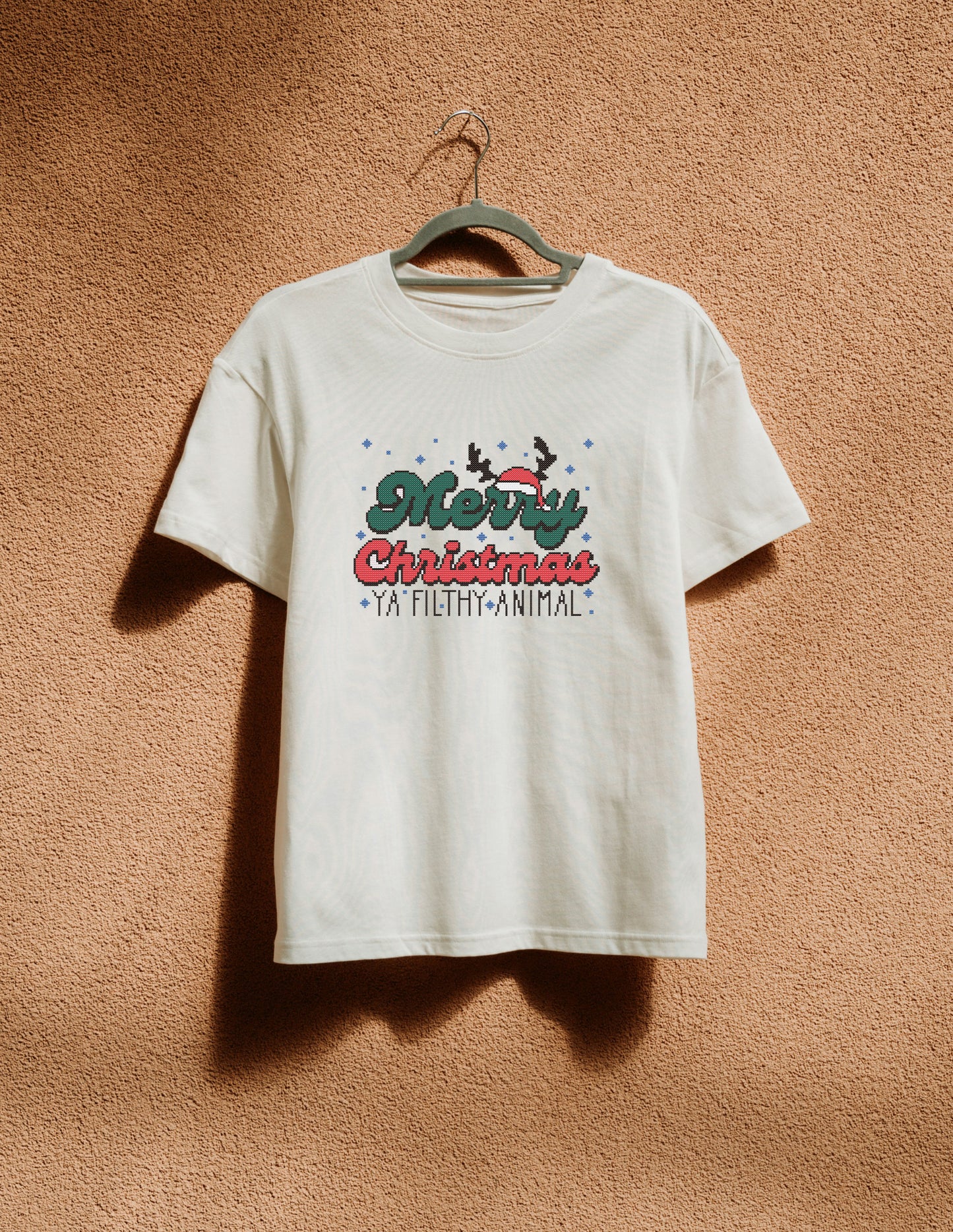 White t-shirt with Christmas design on a hanger against a brown textured wall