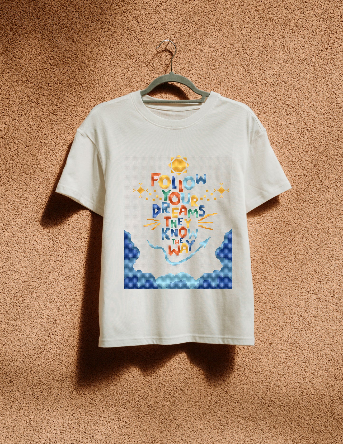 White t-shirt with colorful graphic and text on a hanger against a brown textured wall