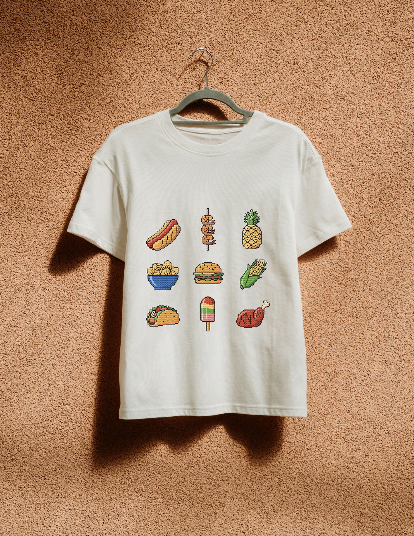 White t-shirt with food illustrations on a hanger against a brown textured wall