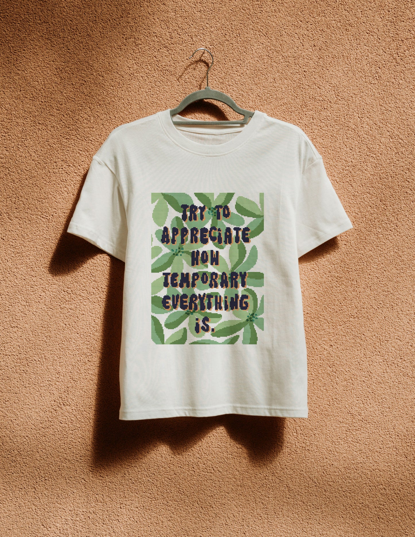 White t-shirt with text and leaf design on a hanger against a textured brown wall