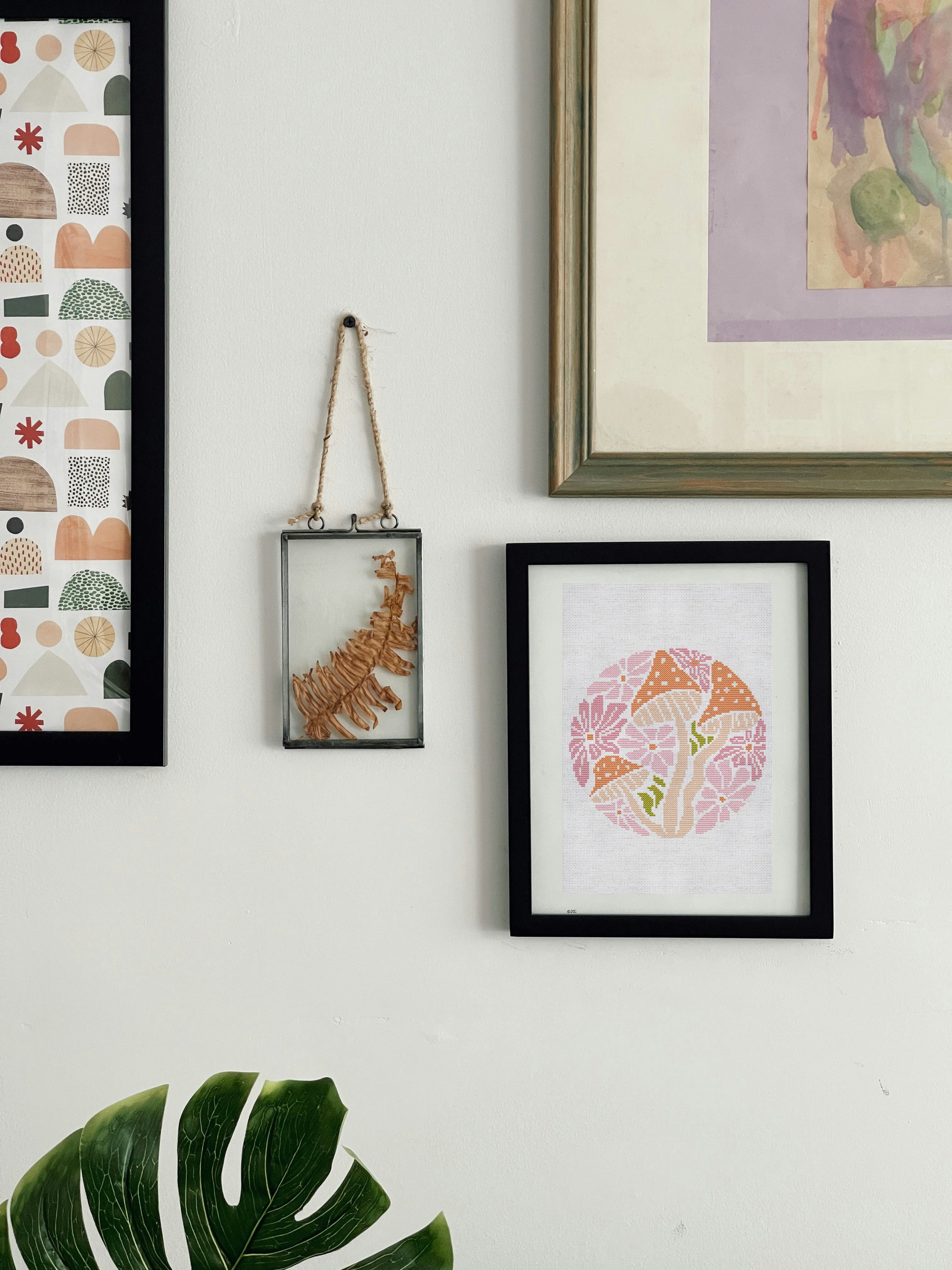 Wall with framed artwork including a colorful abstract piece, a patterned piece, and a black-framed piece with a floral design.