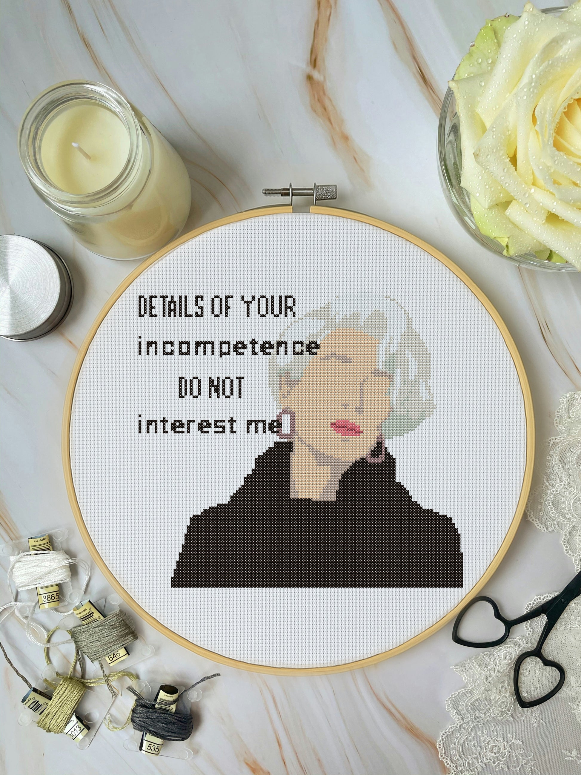 Embroidery hoop with a portrait and text on a marble surface with candles and flowers.