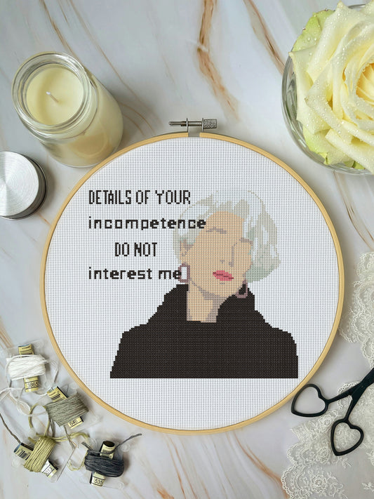 Embroidery hoop with a portrait and text on a marble surface with candles and flowers.