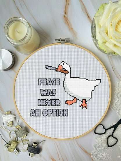 Cross-stitch pattern of a character in an embroidery hoop on a marble surface with a candle and flowers.