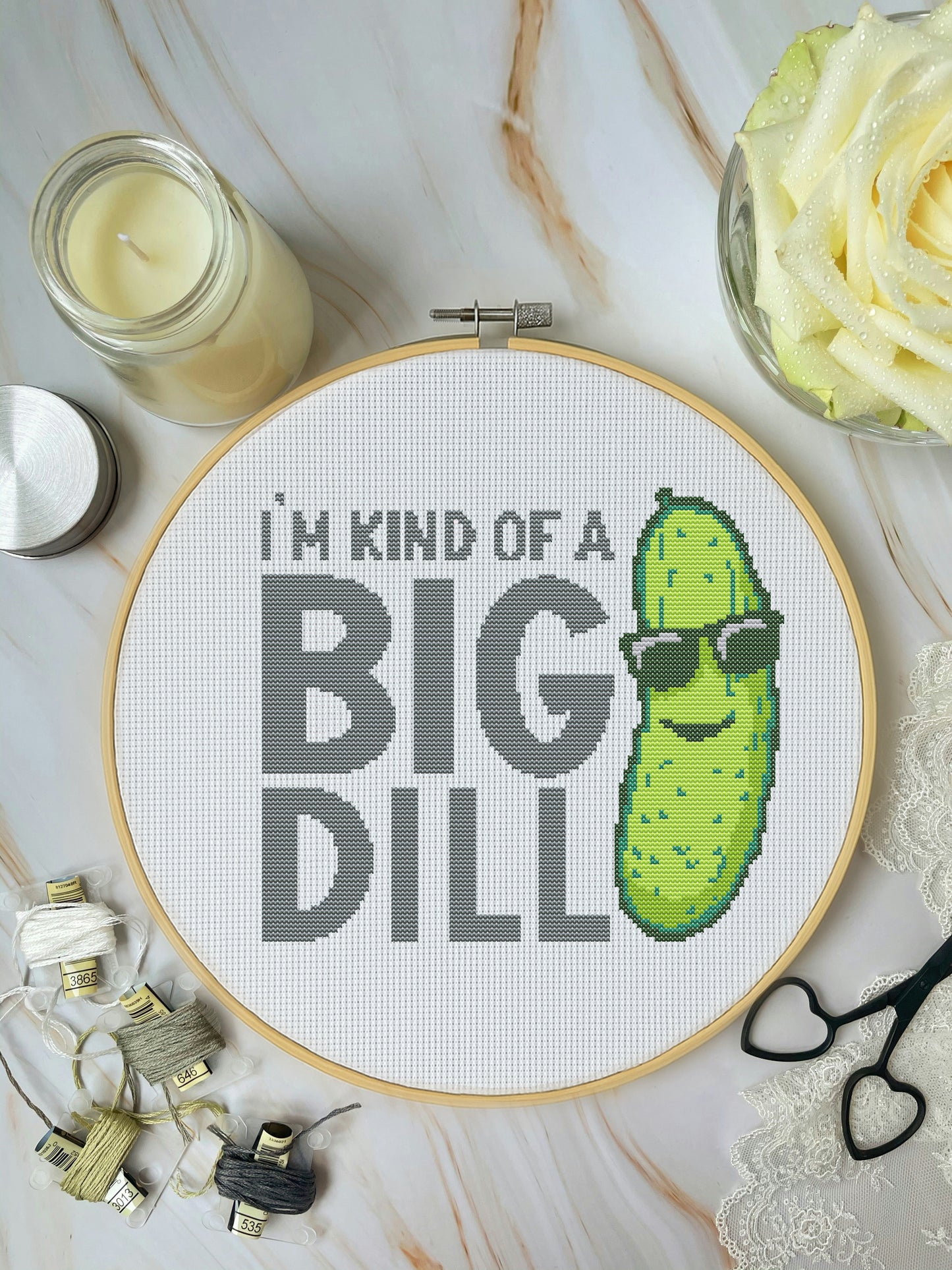 Cross-stitched hoop with a pickle design and text 'I'm kind of a big dill' on a marble surface.