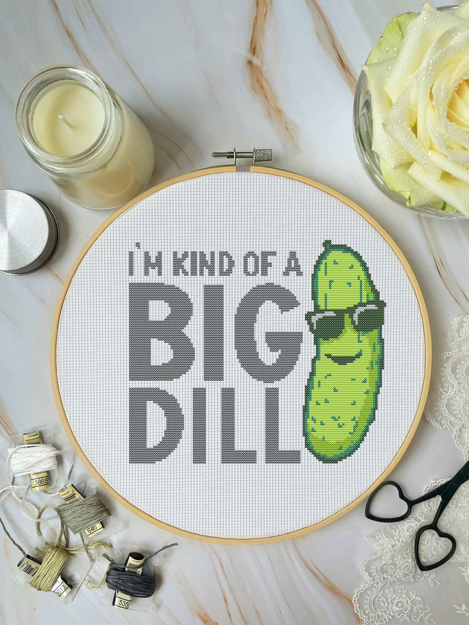 Cross-stitched hoop with a pickle design and text 'I'm kind of a big dill' on a marble surface.