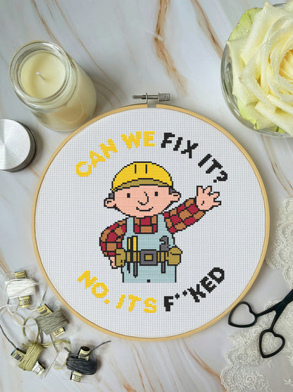 Cross-stitched hoop with cartoon character and text on a marble surface with crafting items.