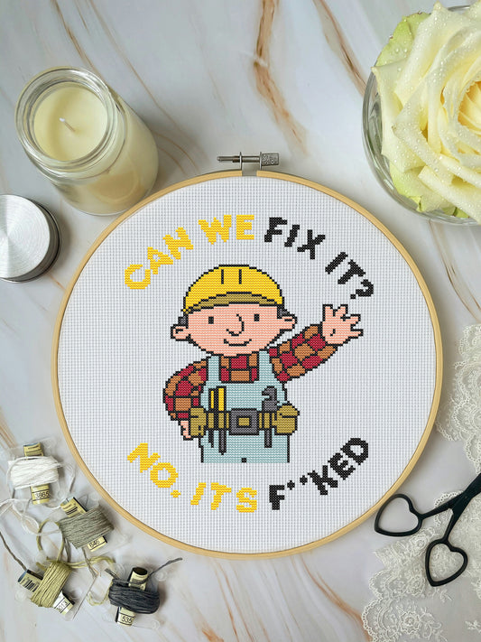 Cross-stitched hoop with cartoon character and text on a marble surface with crafting items.