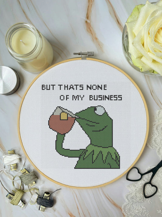Cross-stitched design with text in a hoop, surrounded by crafting materials on a marble surface.