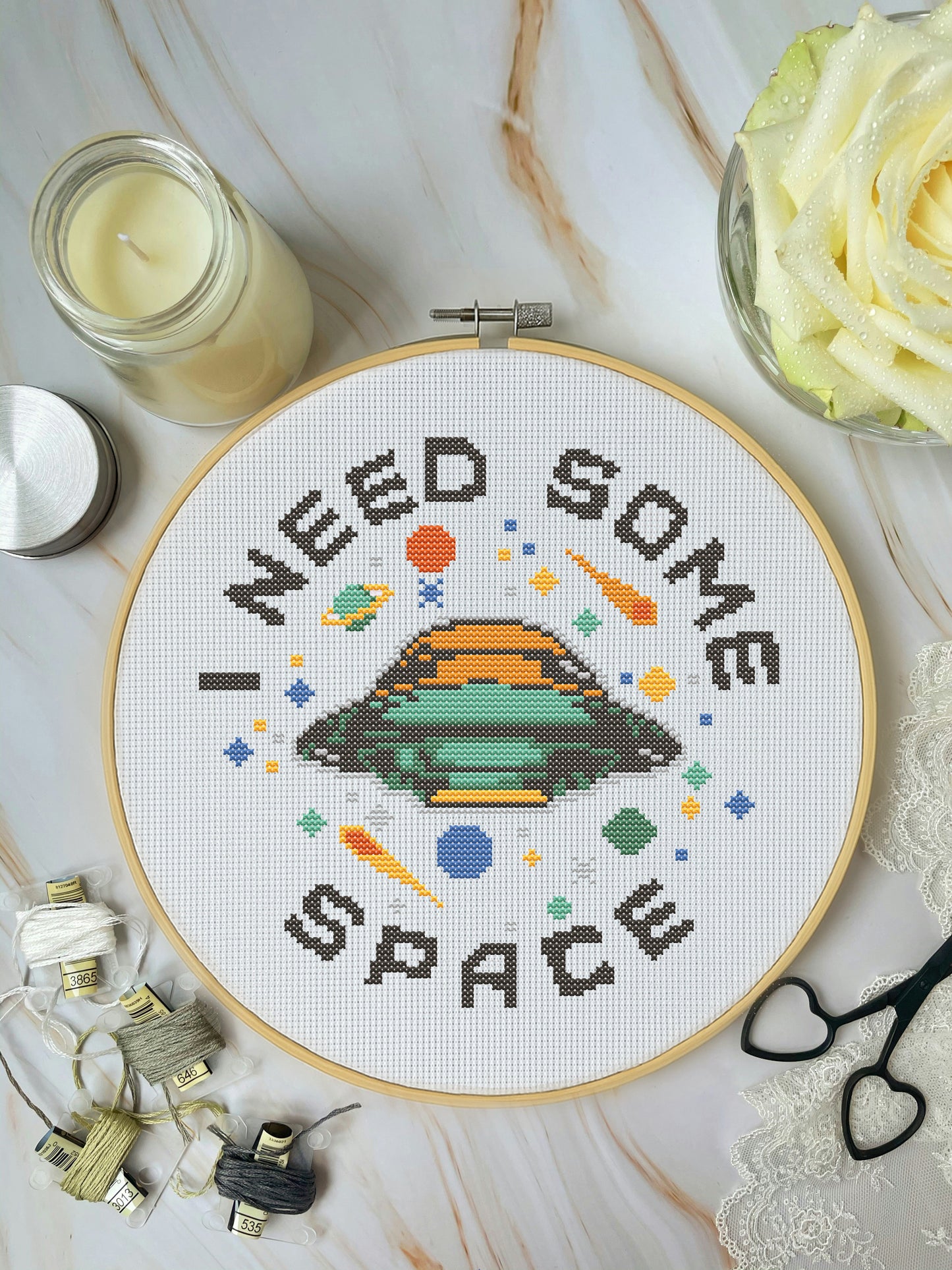 Cross-stitched hoop with 'I Need Some Space' design on a marble surface with candles and flowers.