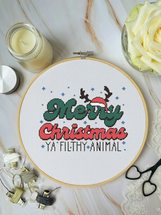 Cross-stitched Christmas design with text on a white background, surrounded by crafting materials.