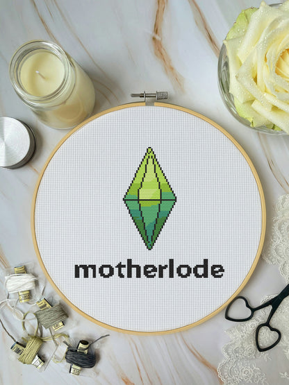 Embroidery hoop with 'motherlode' design on a marble surface with candles and flowers.