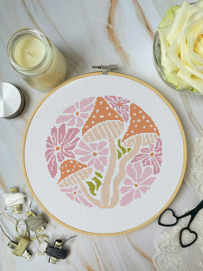 Cross-stitch hoop with floral pattern on a marble surface with sewing supplies.