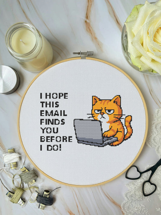 Embroidery hoop with a cat on a laptop and text, surrounded by crafting supplies on a marble surface.