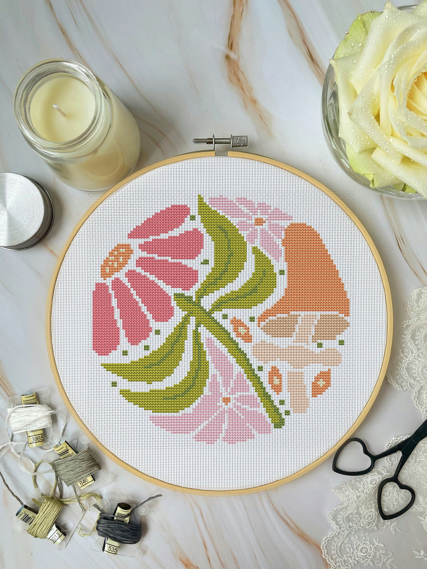 Cross-stitched flower design in a hoop on a marble surface with embroidery supplies.
