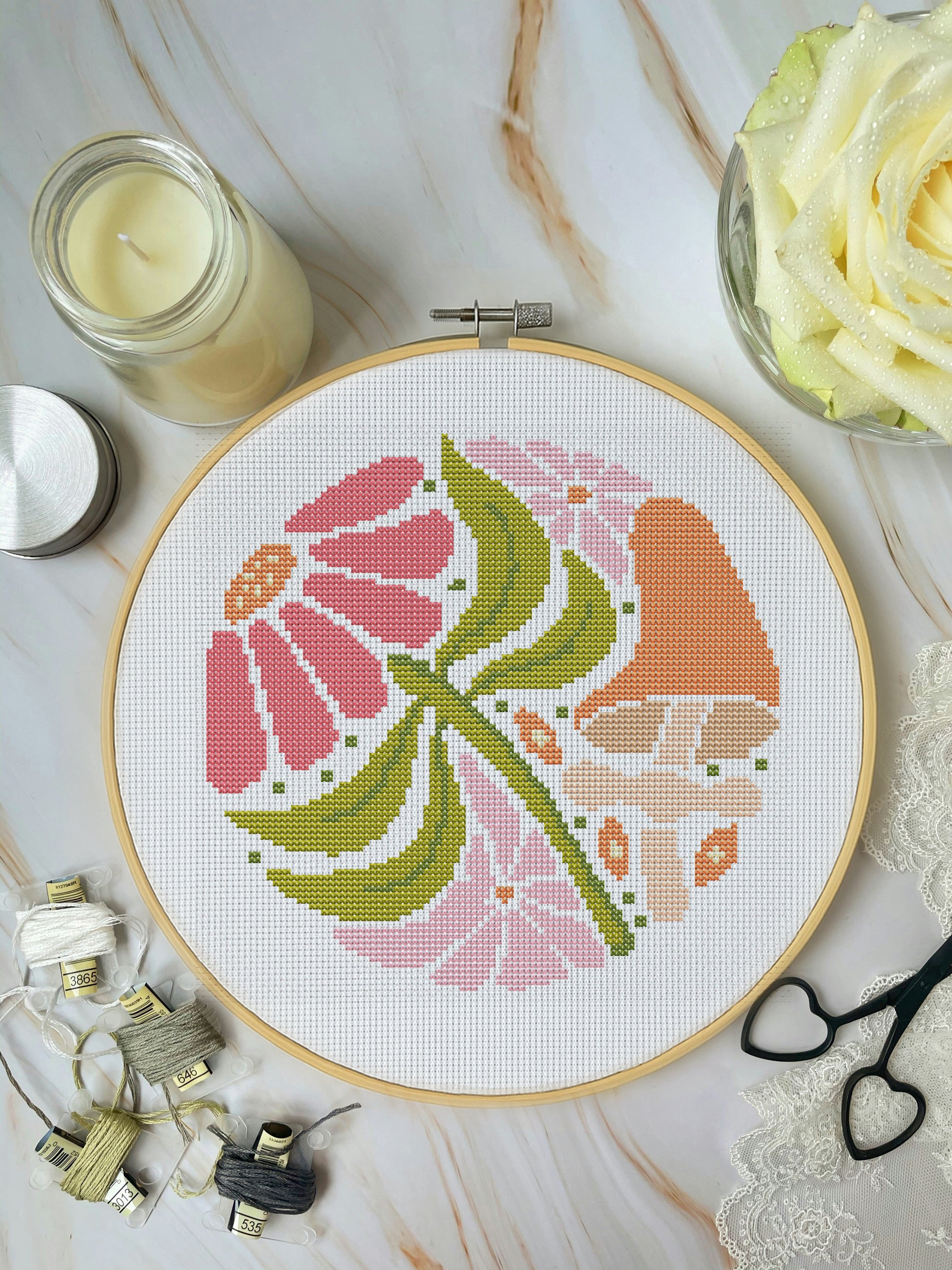 Cross-stitched flower design in a hoop on a marble surface with embroidery supplies.