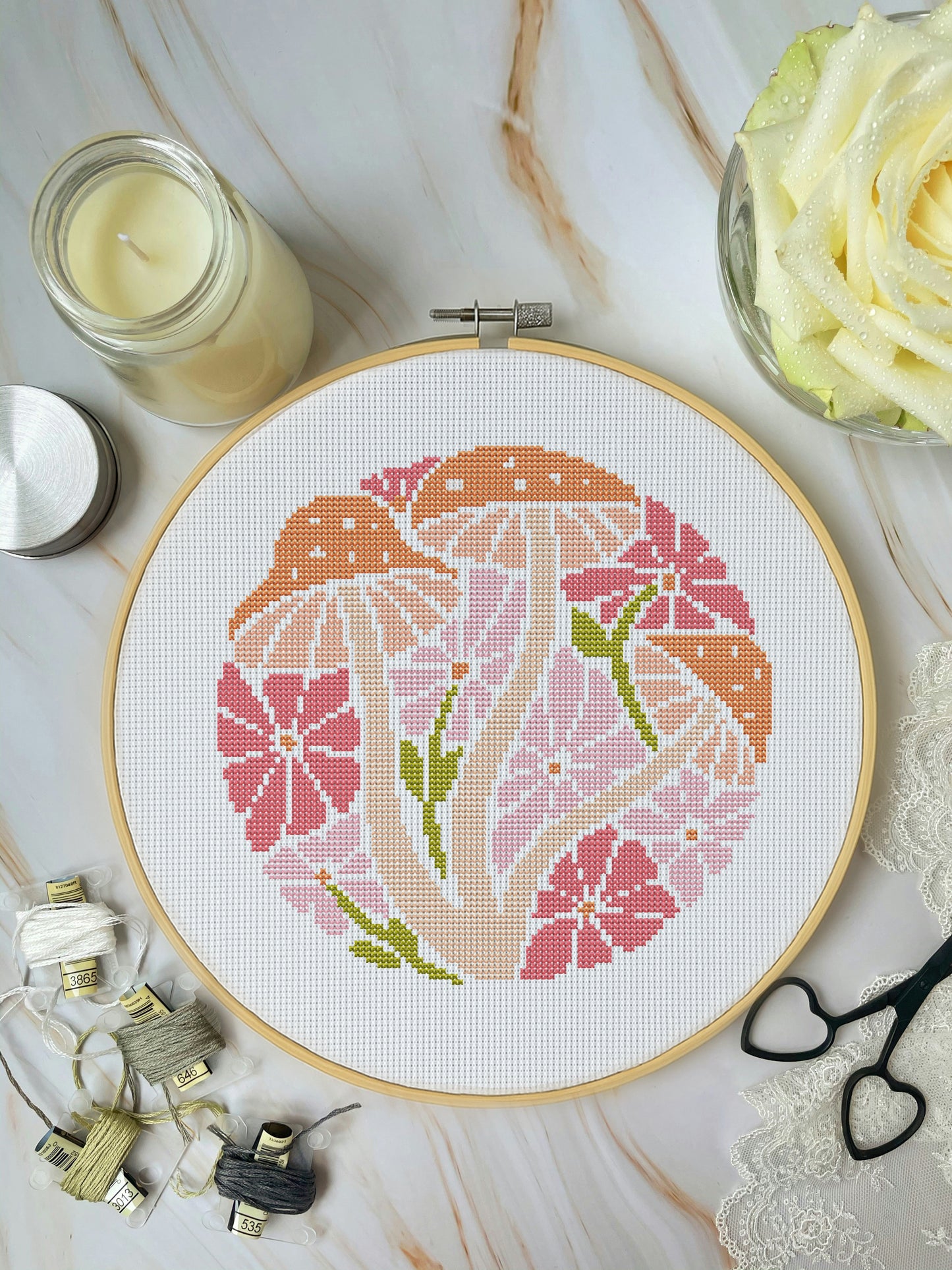 Cross-stitched floral design in a hoop on a marble surface with sewing supplies.