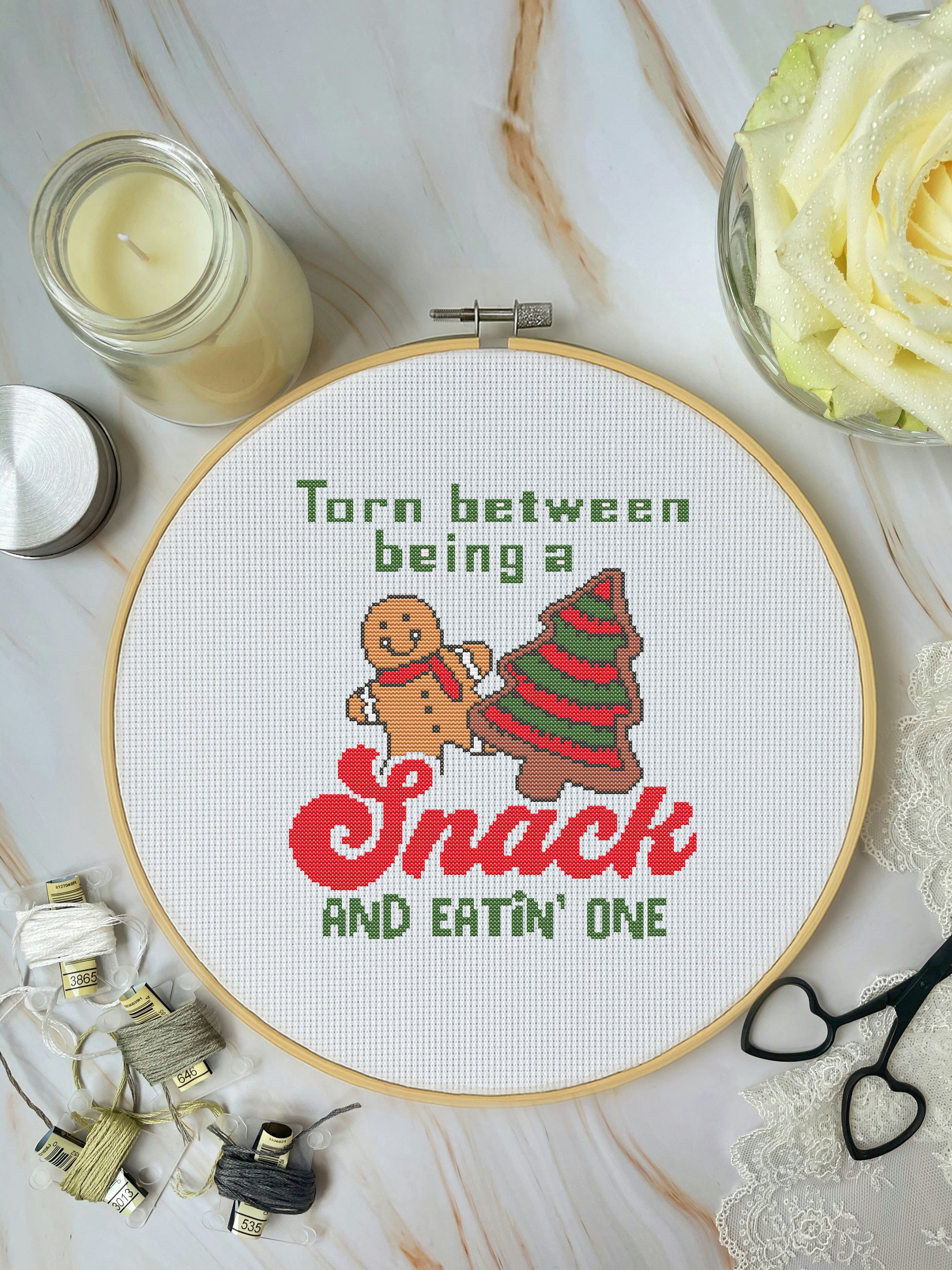 Cross-stitched hoop with Christmas-themed design and text on a marble surface.