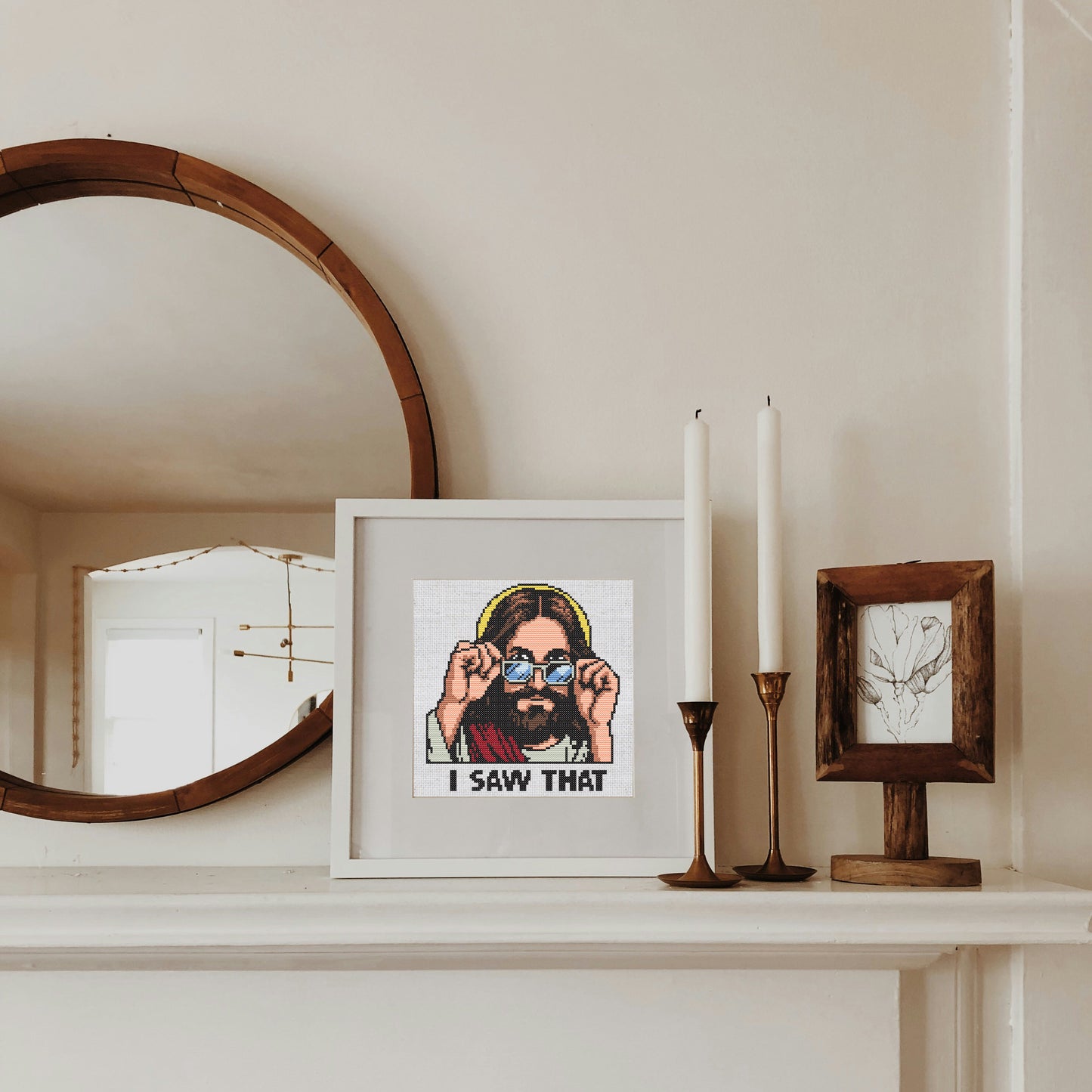 Framed artwork on a mantelpiece with candles and a mirror.