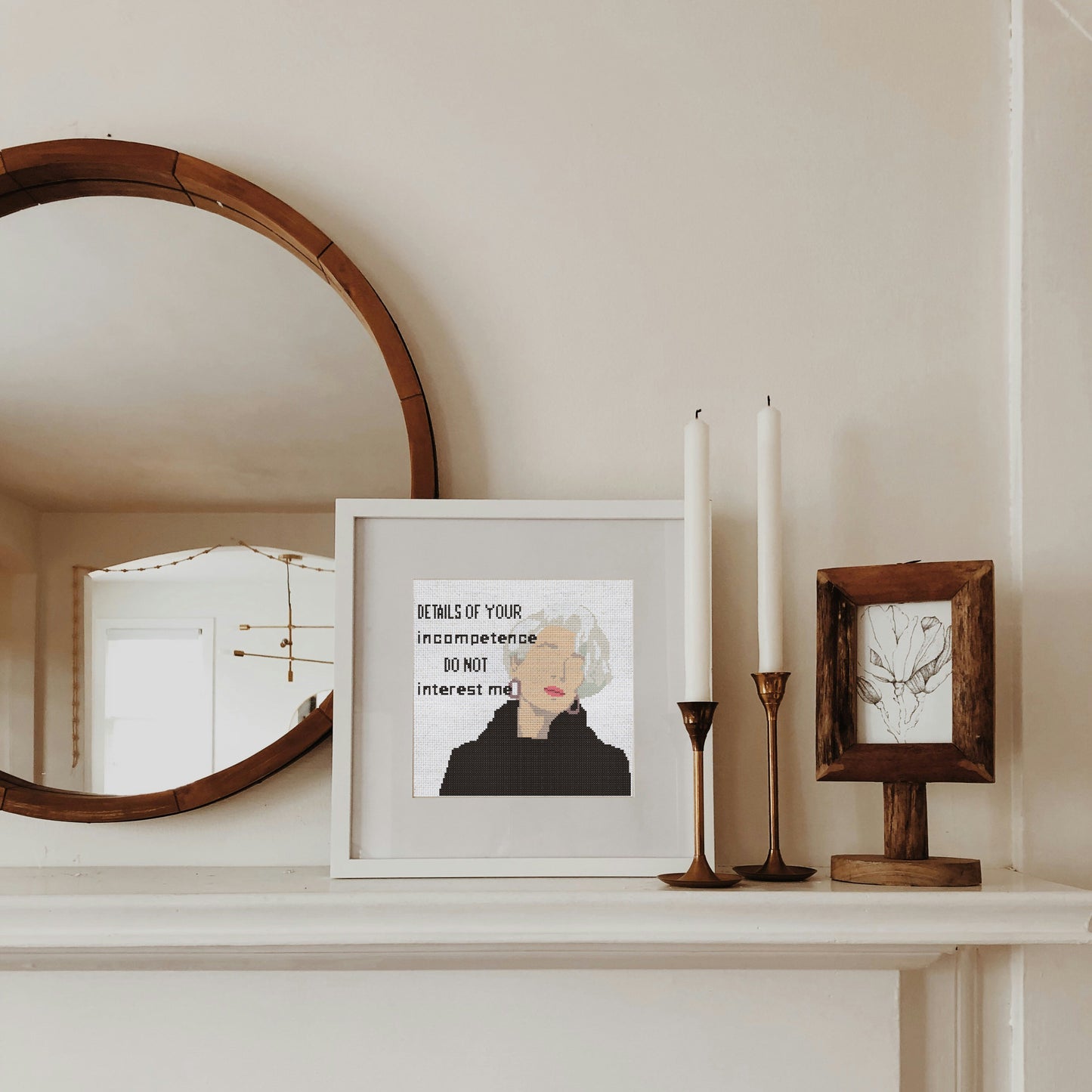 Framed artwork on a shelf with candles and a mirror.