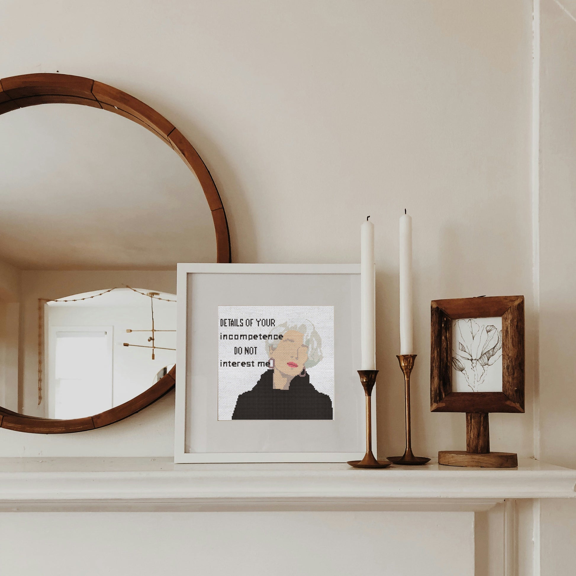 Framed artwork on a shelf with candles and a mirror.