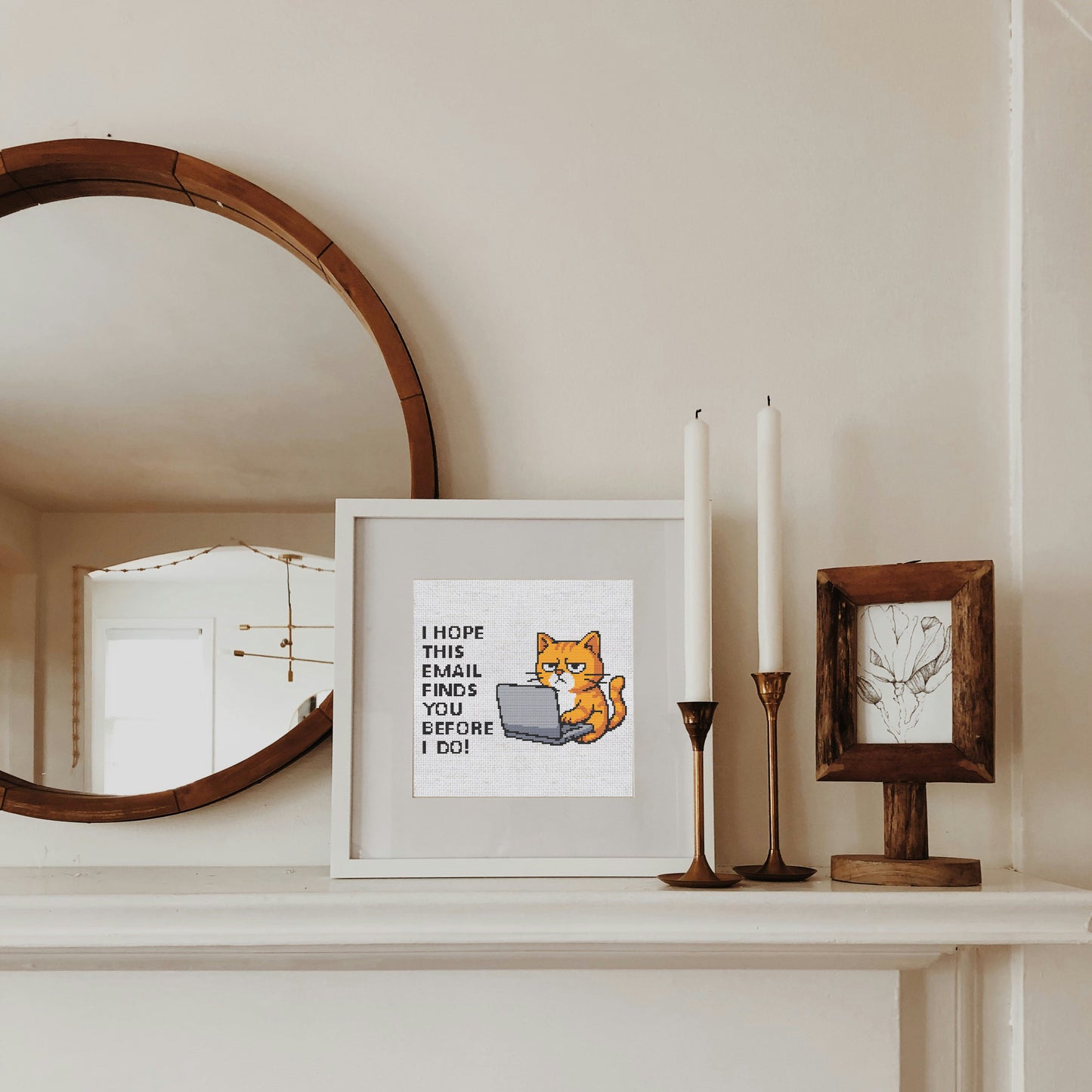 Framed picture of a cat with text on a shelf with candles and a mirror.