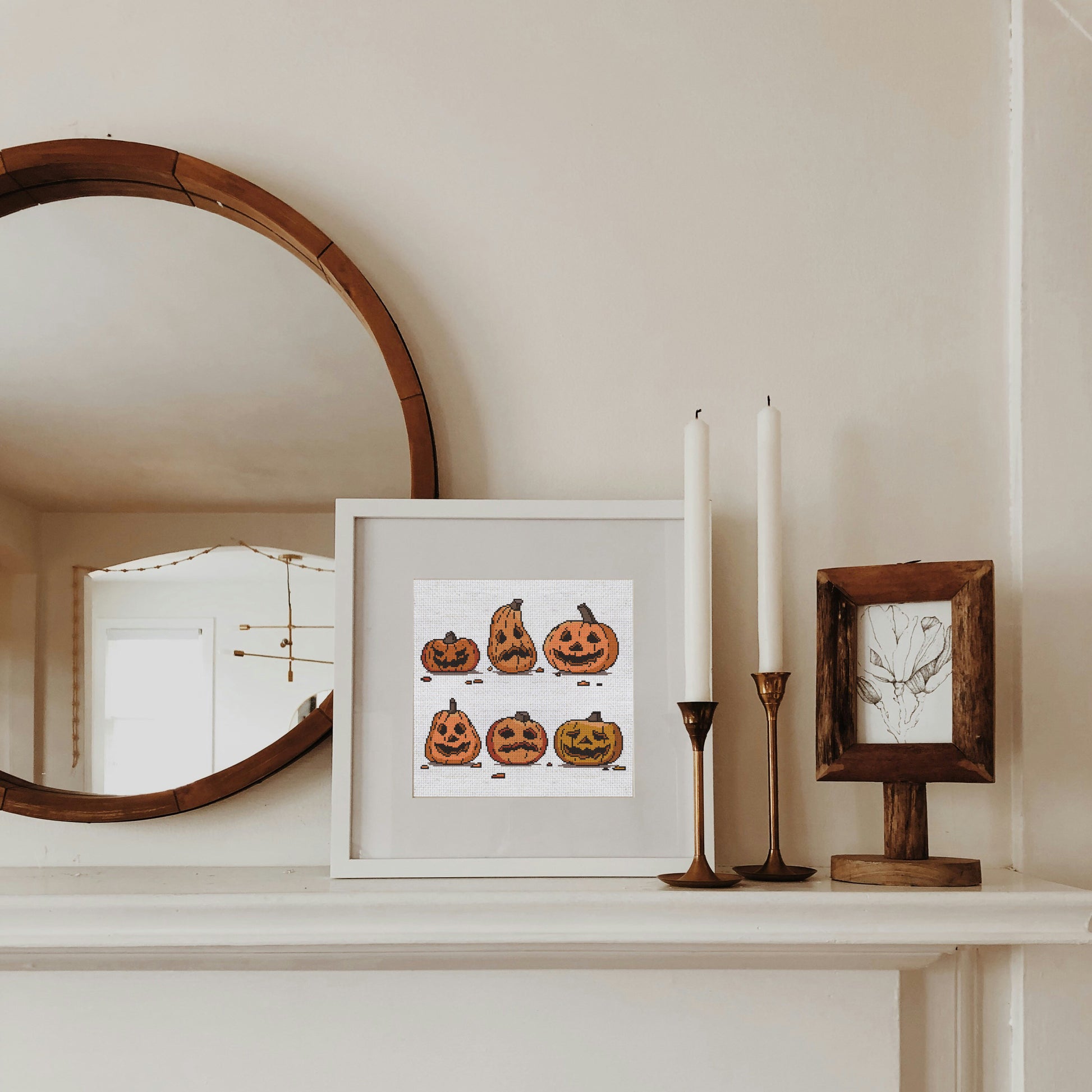 Framed artwork of pumpkins on a mantelpiece with candles and a mirror.