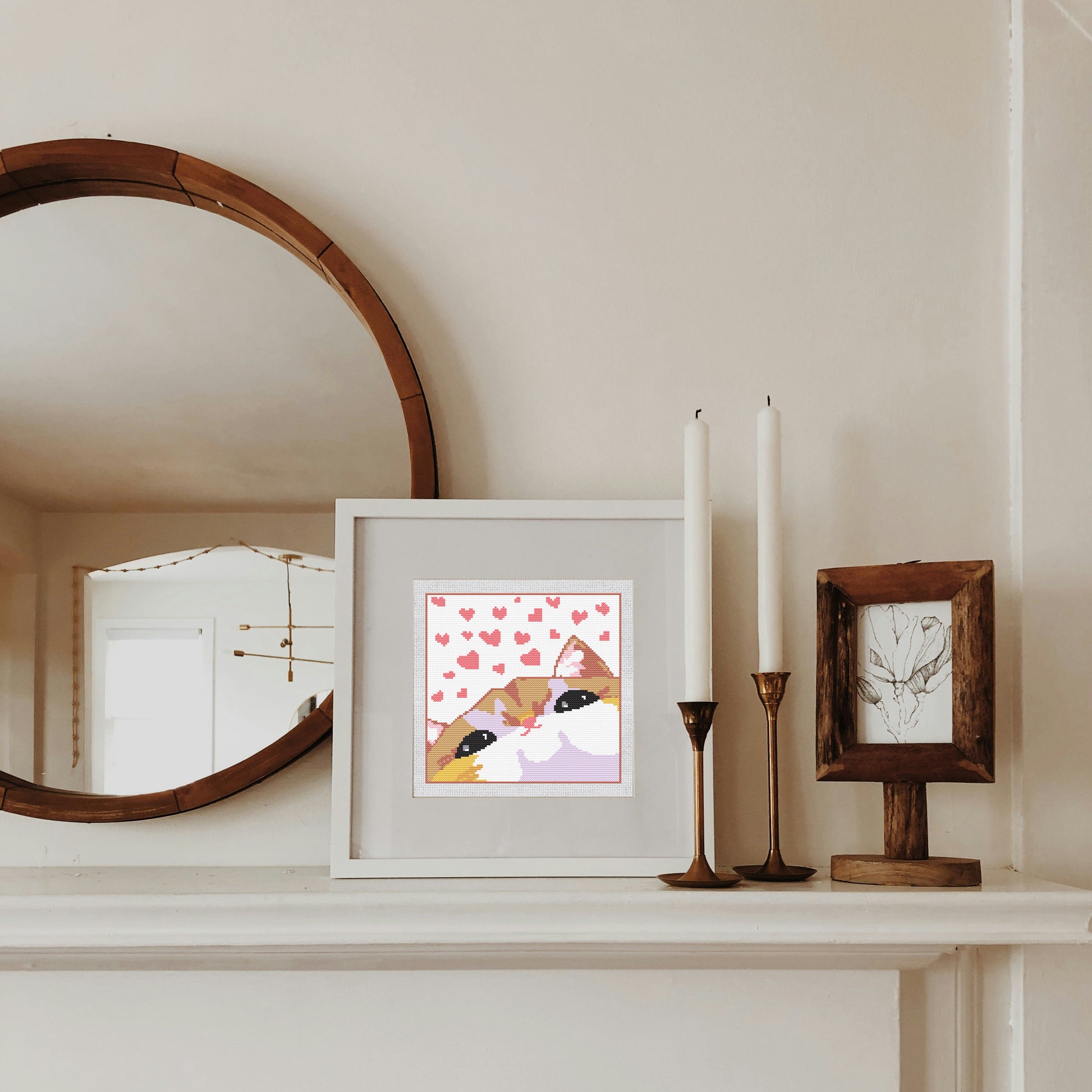 Framed artwork with a cat illustration on a shelf with candles and a mirror.