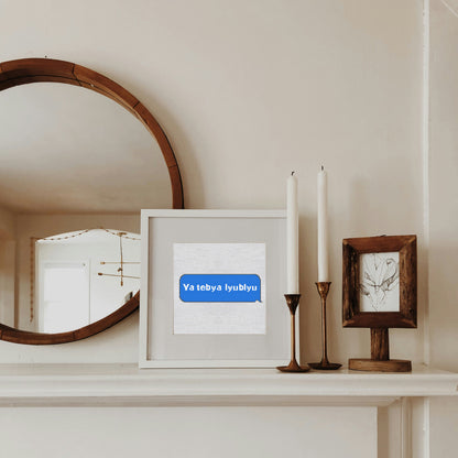 Decorative shelf with a mirror, framed picture, candles, and a small frame against a white wall.