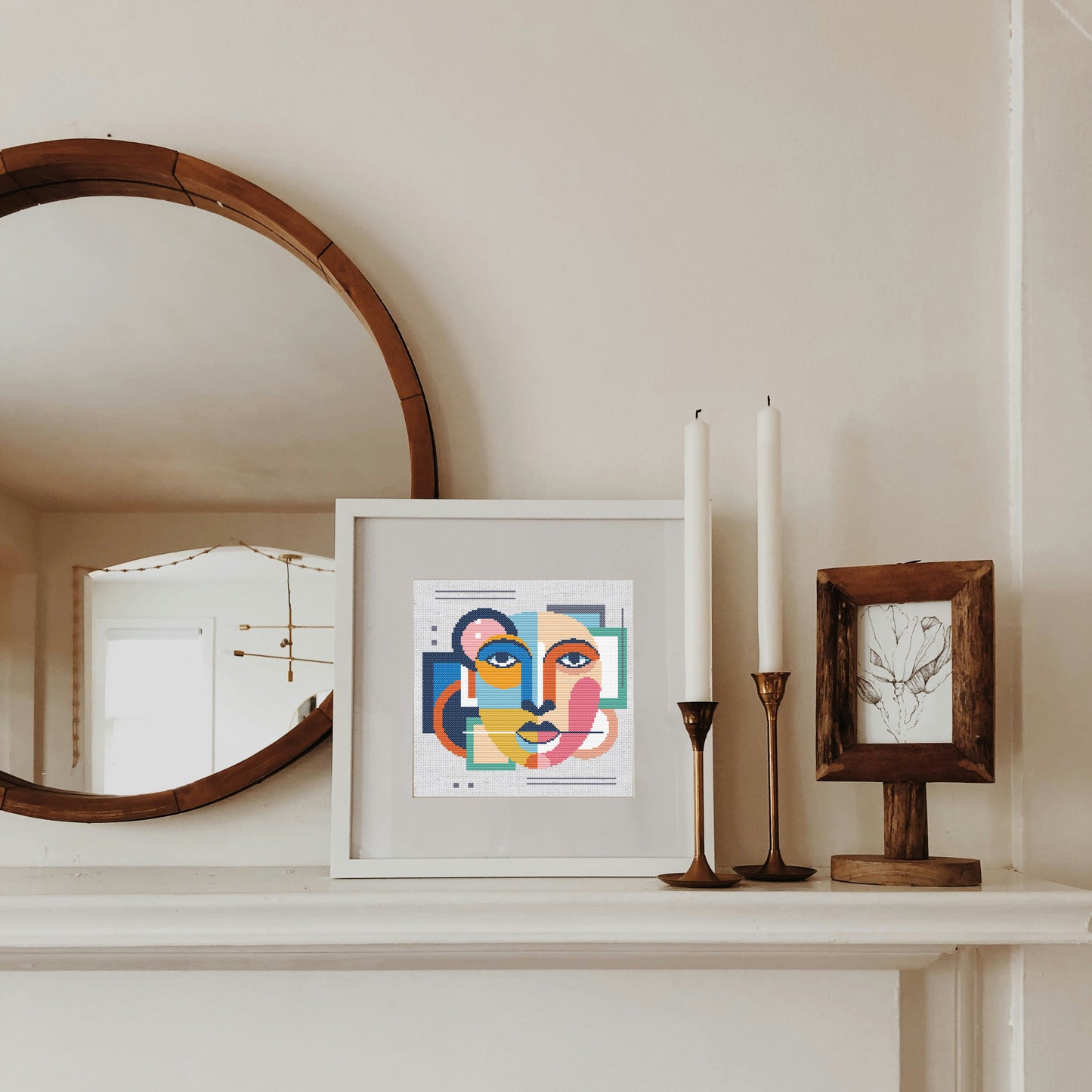 Framed artwork on a mantelpiece with candles and a mirror.