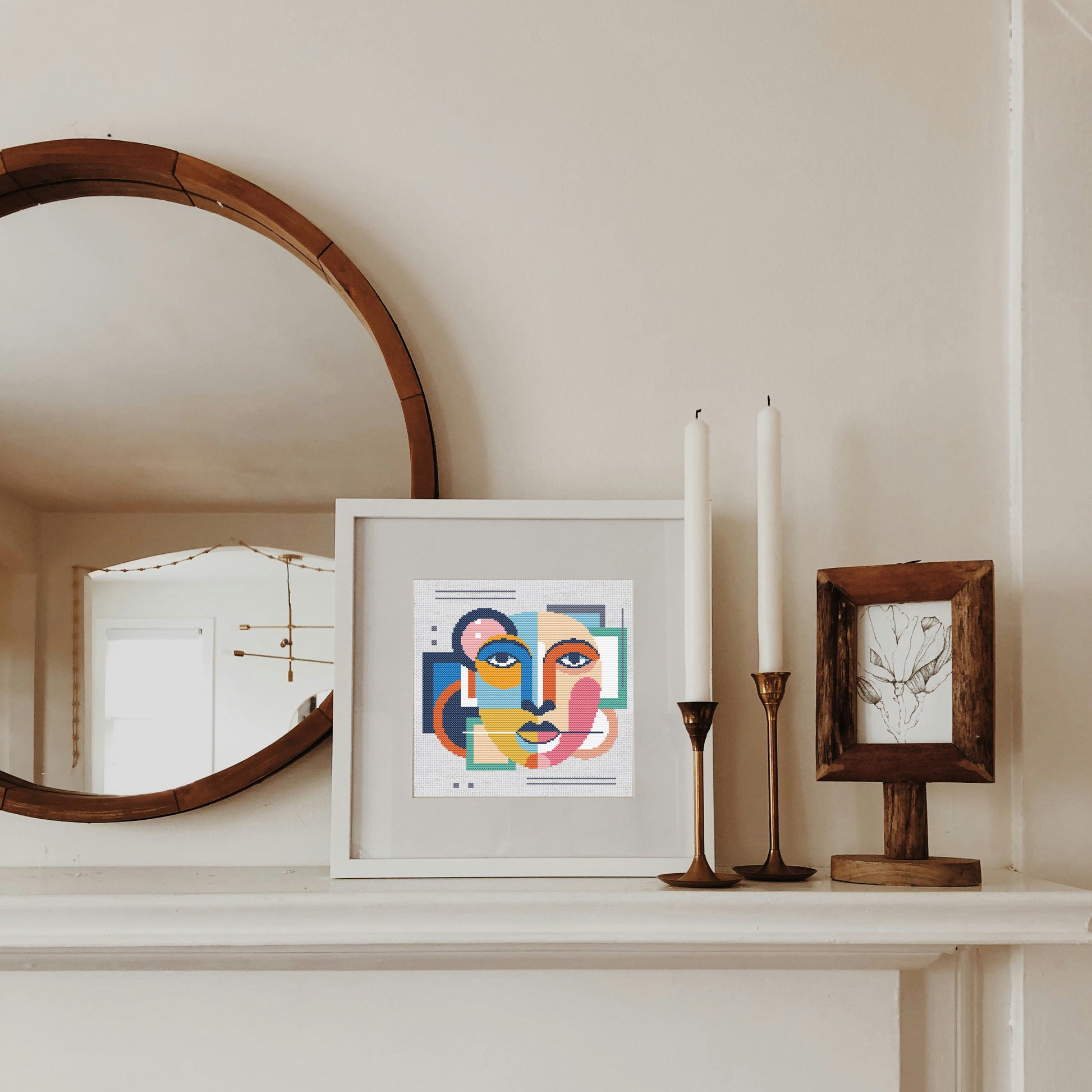 Framed artwork on a mantelpiece with candles and a mirror.