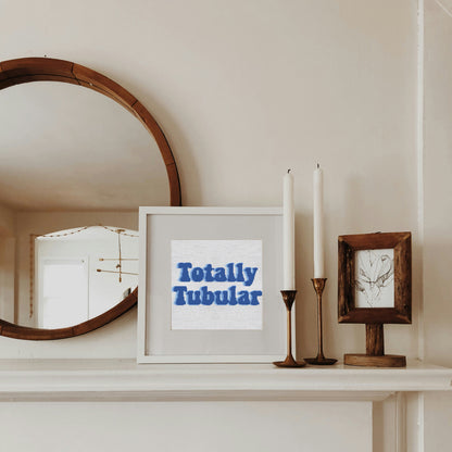 Framed picture with 'Totally Tubular' text on a shelf with a mirror and candles.