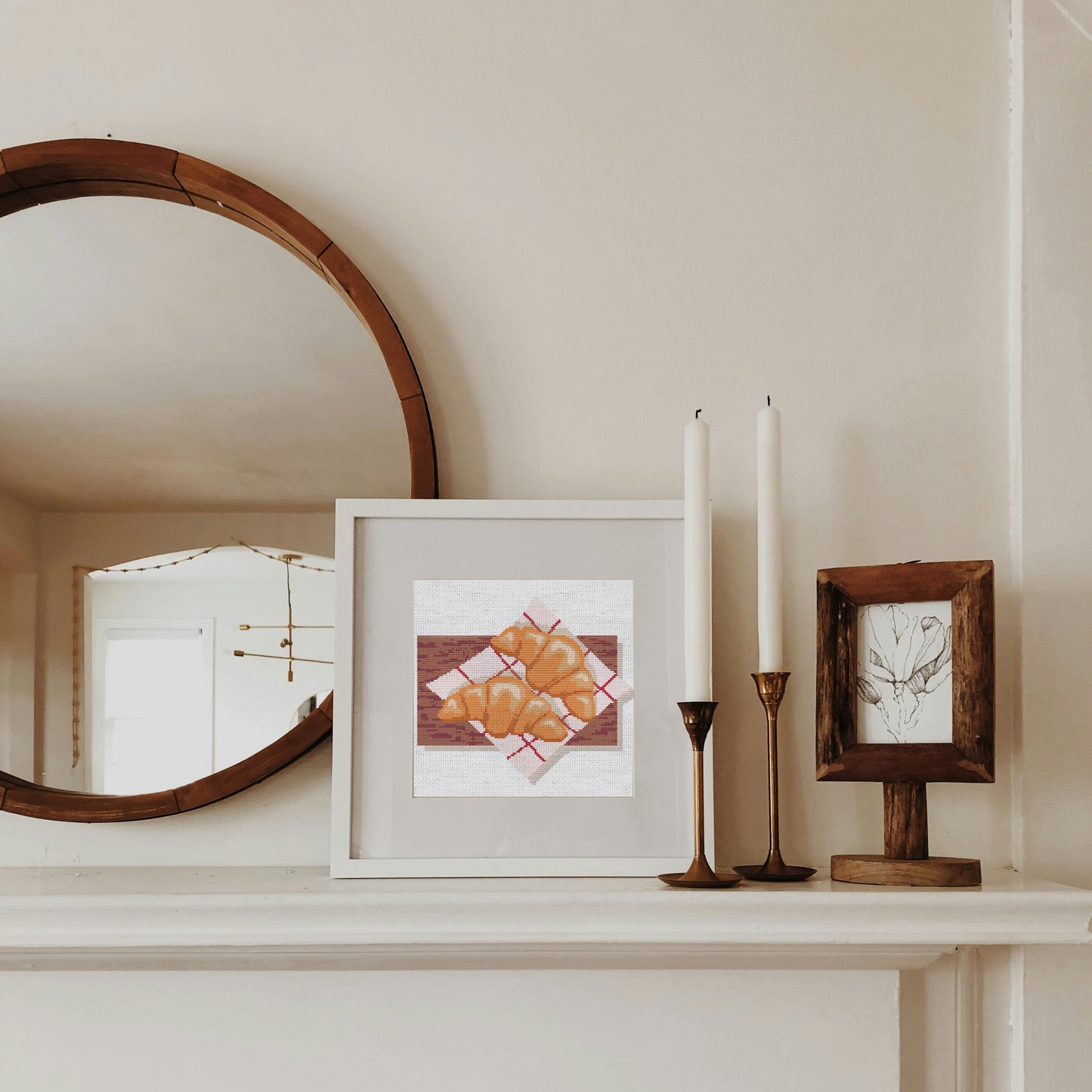 Framed artwork on a mantelpiece with candles and a mirror.