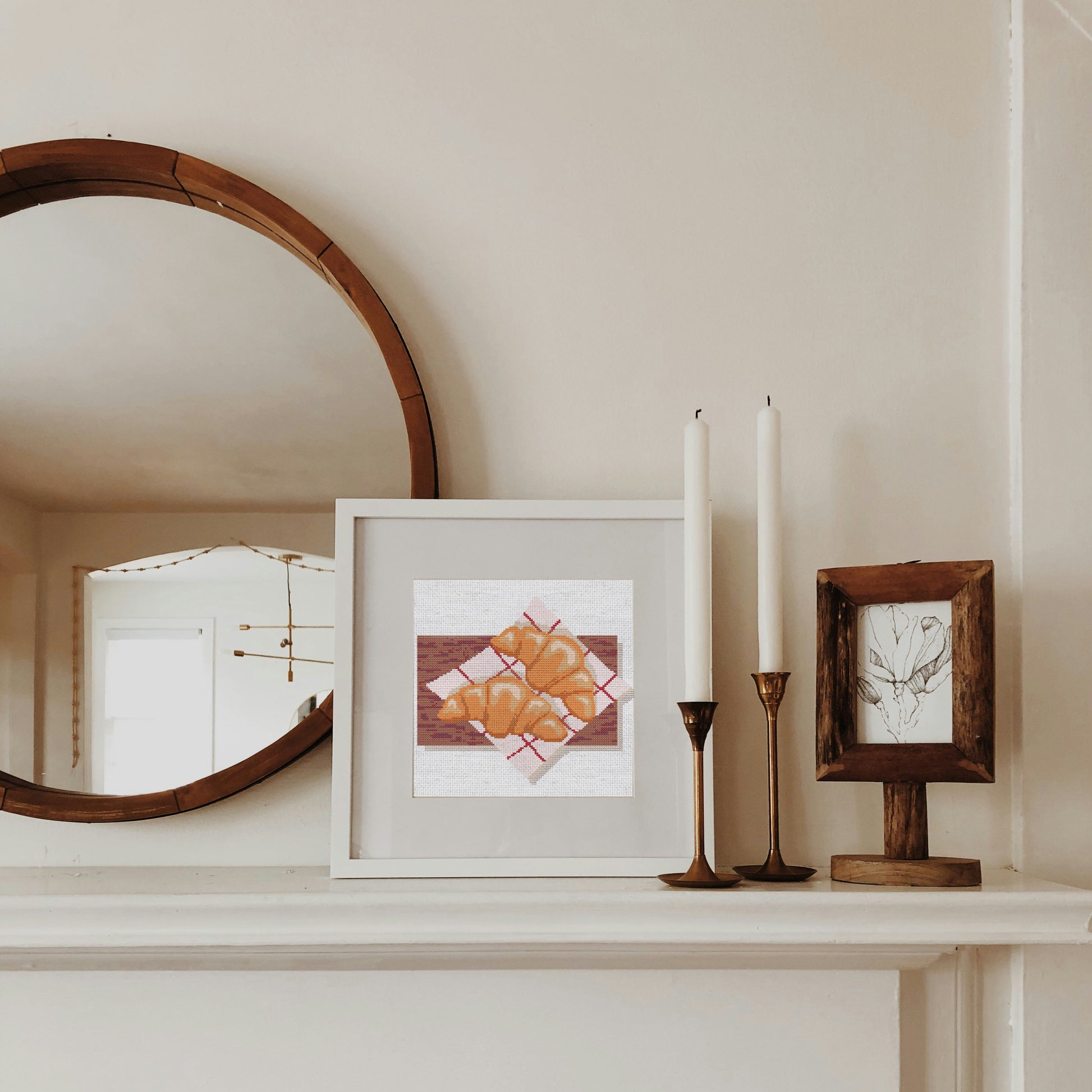 Framed artwork on a mantelpiece with candles and a mirror.