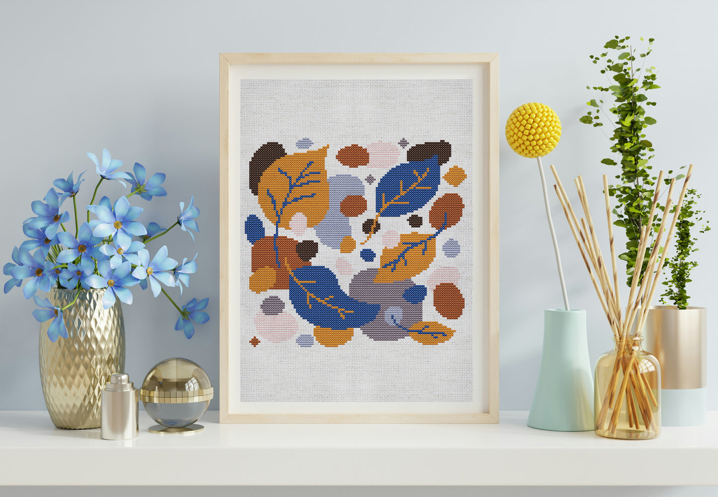 Framed cross-stitch art with abstract floral design on a shelf with decorative items.