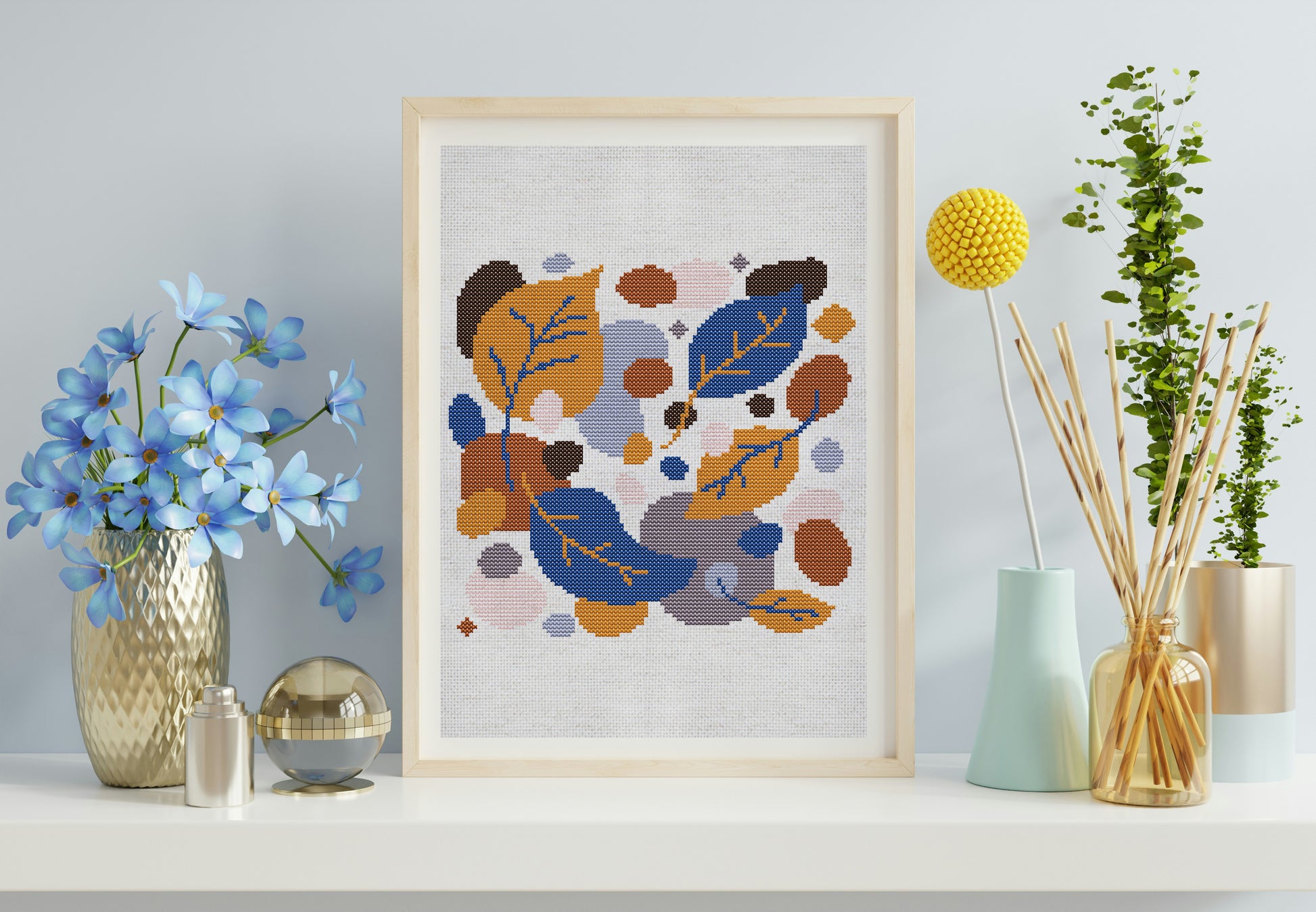 Framed cross-stitch art with abstract floral design on a shelf with decorative items.