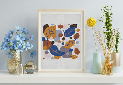 Framed cross-stitch art with abstract floral design on a shelf with decorative items.