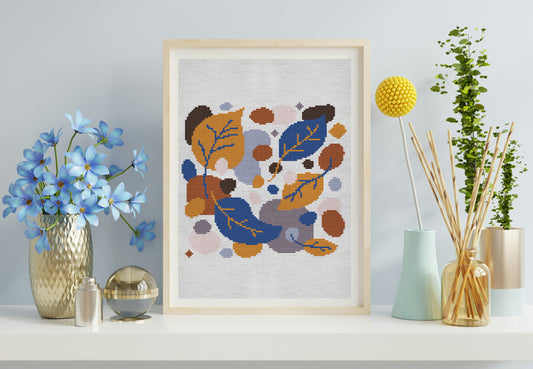 Framed cross-stitch art with abstract floral design on a shelf with decorative items.