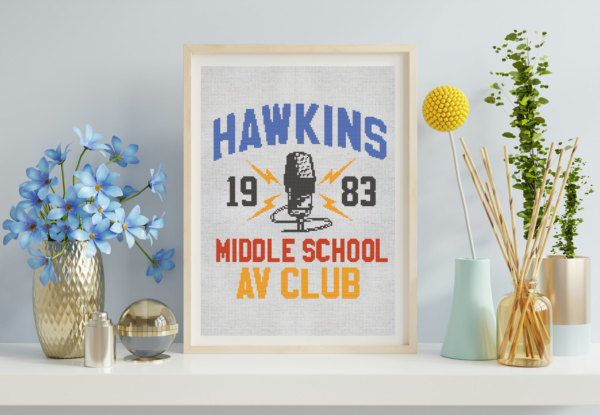 Framed poster with 'Hawkins 1983 Middle School AV Club' design on a shelf with decorative items.
