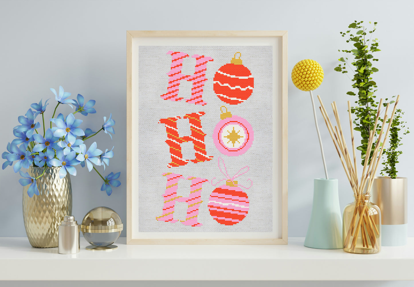 Framed cross-stitched art with 'Ho Ho Ho' and Christmas ornaments on a shelf with decorative items.