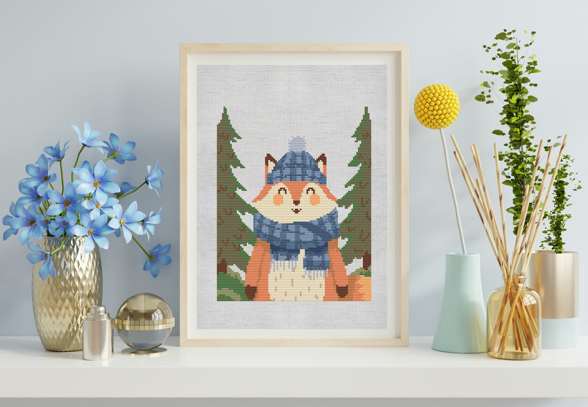 Framed cross-stitch picture of a fox in a forest scene on a shelf with decorative items.