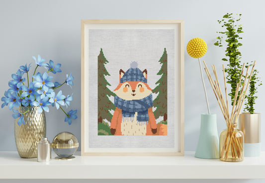 Framed cross-stitch picture of a fox in a forest scene on a shelf with decorative items.