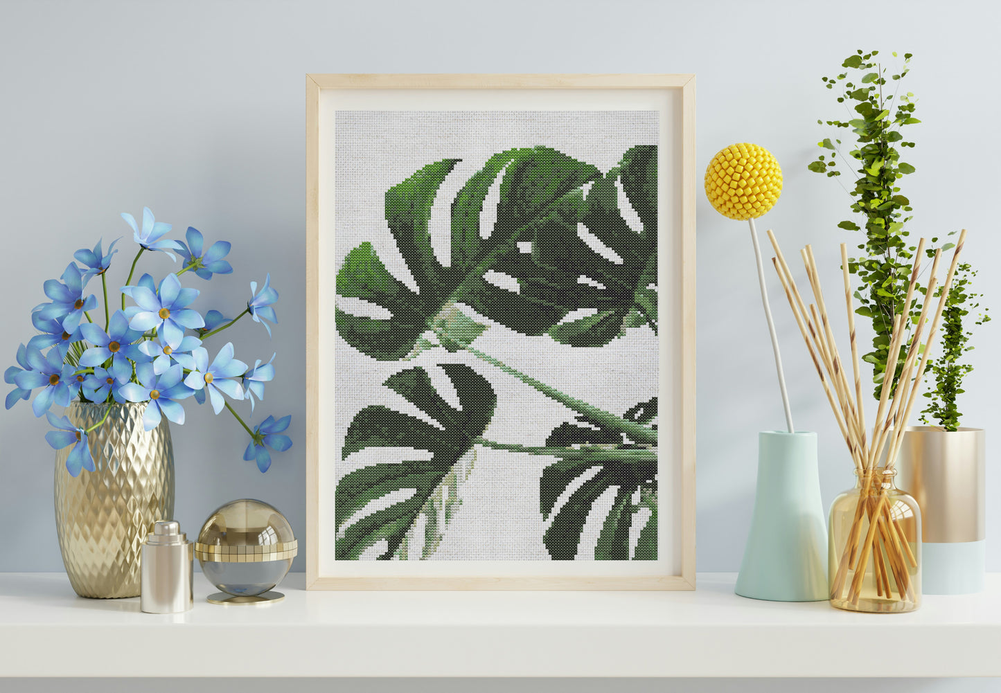 Framed cross-stitch art of a leaf on a wall with decorative vases and plants.