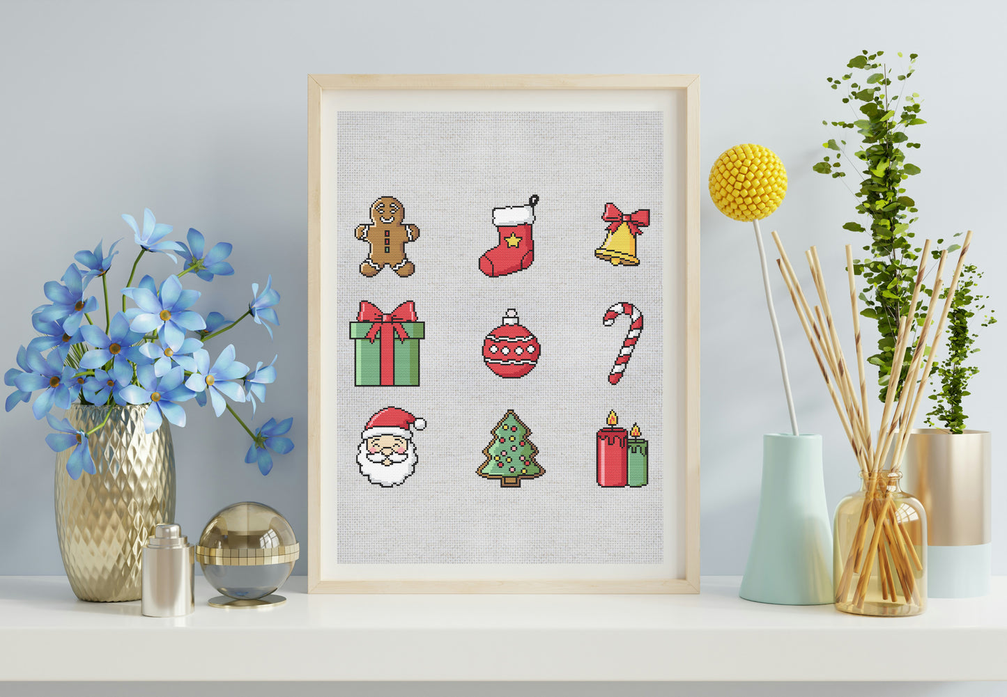 Framed cross-stitch art with Christmas-themed designs on a shelf with decorative items.
