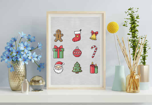 Framed cross-stitch art with Christmas-themed designs on a shelf with decorative items.