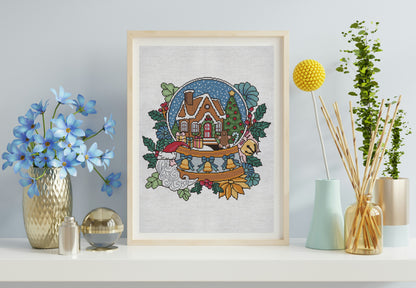 Framed cross-stitch art of a snowy landscape with a house on a shelf with decorative items.